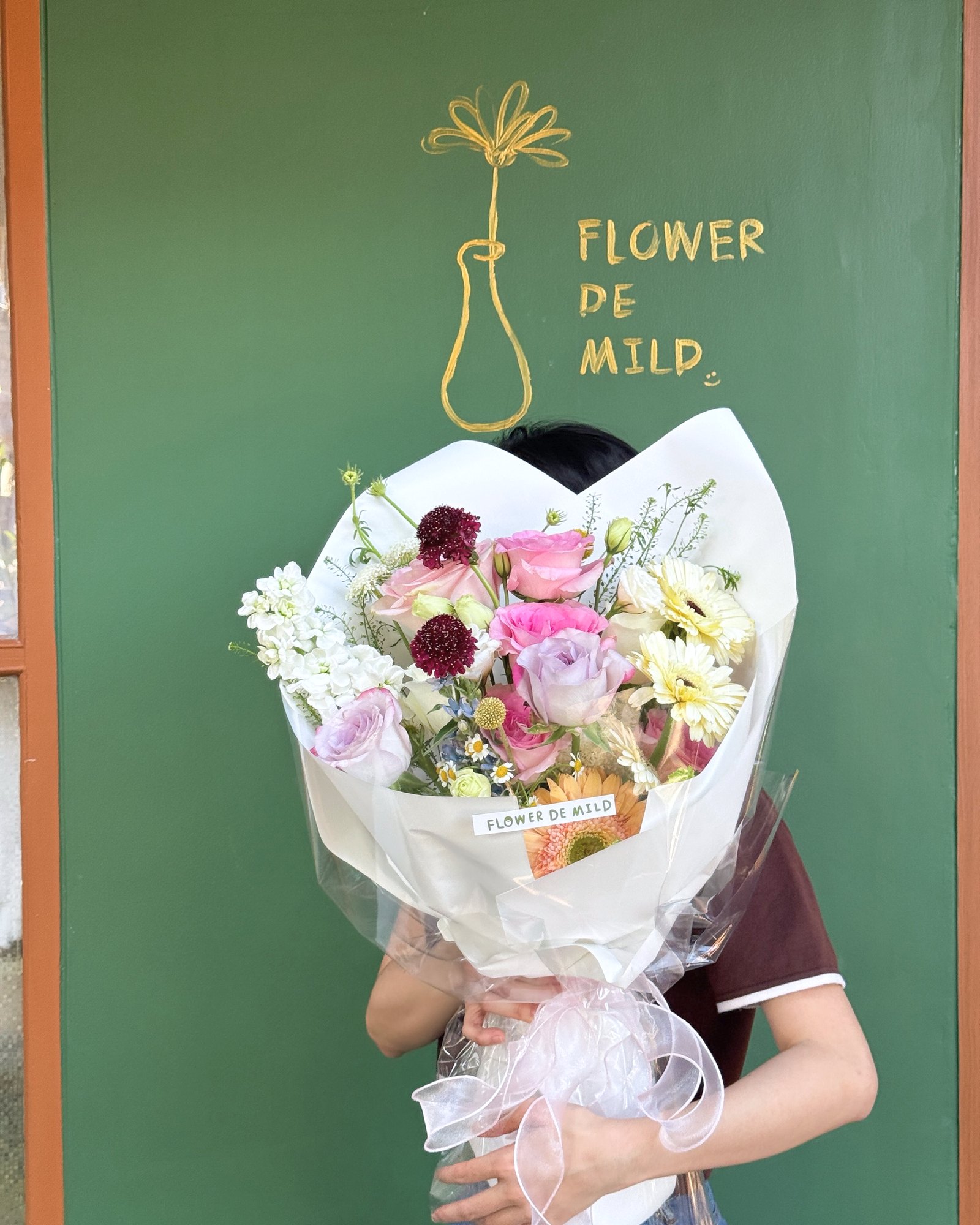 Signature bouquet held in front of the shop's green wall with the painted vase logo